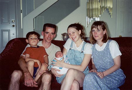 an adoptive family of 5 pose together with their newly adopted baby on a couch